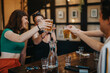 © qunica.com - A group of friends joyfully toasting with beer glasses in a warm, inviting bar. Capturing the spirit of friendship and celebration in a casual atmosphere.