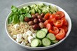 © LimeSky - Colorful nutritious salad bowl featuring quinoa cucumber tomatoes feta olives and basil on a gray backdrop in a white dish Overhead view