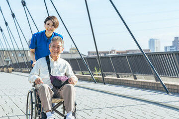 Poster - 介護、車椅子、ヘルパー、介護士、笑顔、歩道、外出、サポート、支援、高齢者、お年寄り、シニア、道路、屋外、女性、男性、日本人、サービス、デイサービス、ホームヘルパー、介護福祉士、老人ホーム、障害、障がい者、介護員、青空、元気、ポジティブ、街、都市、社会、橋、ウェルネス、リハビリ、健康、老後、明るい、散歩、外出レク、福祉、老人、押す、スタッフ、フレイル、サルコペニア、ADL、デイケア、施設、カメラ目線