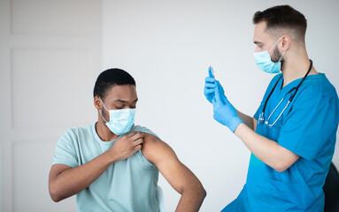 Poster - Covid-19 vaccination program. Black male patient getting coronavirus vaccine shot on visit to physician at health centre. African American guy being immunized against global virus