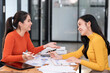 © NAMPIX - Two young Asian business woman talking, consulting and discussing working with new startup project idea presentation in the office.