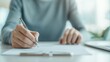 © kokoson6 - person writing on document with pen, focused on their task. setting is bright and modern, suggesting professional environment