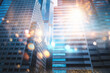 A low angle view of tall office buildings reaching towards a bright sun with a lens flare.