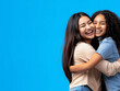 © Digital Sensei - Two Asian girls hugging and smiling isolated on a blue background