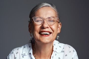 Senior woman, glasses and happy in studio for positive attitude, confidence and joy on gray background. Elderly person, smile and cheerful for gratitude, retirement and good mood with fun or laughing