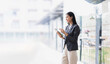 © SOMKID - Asian businesswoman holding tablet standing in office.