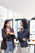 © SOMKID - Two Asian business female talking to partner standing in office.