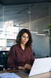 © Stock 4 You - Young professional it specialist latin hispanic business lady working on laptop pc sitting at desk in modern office space. Middle eastern indian woman using computer technology app for work. Vertical