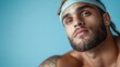 © JoxyAimages - A muscular man with a headband and tattoos, exudes intensity and determination with his piercing gaze against a solid blue background, wearing athletic gear.