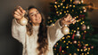 © polinaloves - Young woman in white sweater decorating Christmas tree in a cozy room.