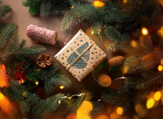 Poster - A wrapped gift with a brown paper and blue and white design sits on a brown surface, surrounded by pine branches and a string of lights.
