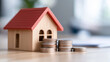 © NaphakStudio - wooden house model with red roof sits beside stacks of coins, symbolizing savings and investment in real estate. image conveys financial growth and home ownership.