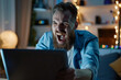 © Alberto Gonzalez  - Ecstatic man celebrating a victory while looking at a laptop screen in a room with ambient lighting.