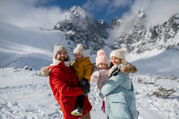 Wall Mural - Young family is enjoying winter holiday in the mountains, standing in the middle of snowy landscape.