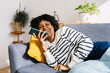 © Xavier Lorenzo - Happy young Latin American woman relaxing on sofa sending a voice note audio message on mobile phone while enjoying cozy winter day at home