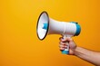©  S u n n y B u n n y - Hand holding megaphone against vibrant orange background for communication and announcement themes