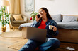 © Bliss - The young woman sits comfortably on the floor, laughing on the phone while sipping coffee and working on her laptop.
