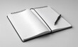 © Miklos - A black spiral notebook sits open on a white desk with a black pen lying on the right page