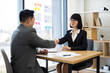 © sofiko14 - Caucasian businesswoman and Asian businessman shaking hands in modern office setting. Business professionals reaching agreement, sealing contract, partnership success symbolized.