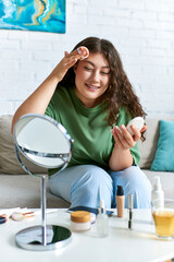 a young and curly plus size woman applies skincare products in her cozy living room, enjoying her be