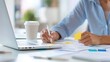 © Vilaysack - woman using sticky notes for planning and organization at a desk with a laptop and coffee cup, representing productivity in a bright office environment.