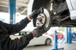 © SerPak - A skilled mechanic is carefully installing a brake rotor on a vehicle at an auto repair facility. The workspace is well equipped, with multiple cars visible in the background, showcasing an active rep