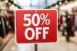 © JAKE STUDIO - A vibrant red sign displays '50% OFF' in a clothing store, highlighting a sale and attracting shoppers.
