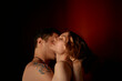 © Connect Images - Close-up of a man and woman embracing and kissing against a dark background with warm lighting.