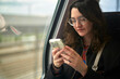 © Connect Images - Woman with glasses using a smartphone on a train.