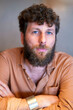 © Connect Images - Bearded man with curly hair looking at the camera with a neutral expression, wearing a light brown shirt and a silver bracelet.