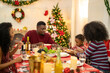 © ultramansk - A warm Christmas family dinner with a father serving food to his young child, surrounded by festive decorations, a Christmas tree, and a holiday table spread. Joyful and cozy holiday atmosphere.