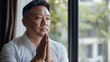© Lion - Asian man praying quietly, hands clasped, natural daylight from a nearby window, peaceful and minimalistic setting