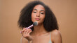 © Yuliia - African American woman applying powder make-up natural beauty clean soft moisturized hydrated skin care treatment girl make blush on face bronze contouring using makeup brush cosmetic beige background