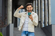 © Andrii Iemelianenko - Amazed Indian man use mobile smartphone celebrating win good message news, lottery jackpot victory giveaway online outdoors. Happy Arabian Hindu guy in downtown city street. Business people lifestyles