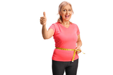 Wall Mural - Mature woman measuring her waist with a tape and gesturing thumbs up, weight loss concept