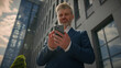 © Yuliia - Mature senior employer middle-aged Caucasian entrepreneur outdoors old business man looking at mobile phone thinking pensive ponder idea solution think male businessman in city browsing smartphone