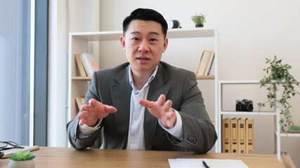 Wall Mural - Asian businessman in modern office engaged in online video call using laptop. Professional setting includes digital charts on wall, subtle lighting, and neat desk setup.