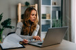 © djile - Businesswoman working with laptop and analyzing documents at home office