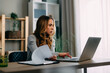 © djile - Young woman working at home office using laptop and analyzing documents
