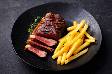 Wall Mural - Beef Steak medium rare with French fries on a black plate. Dark background. Close up.