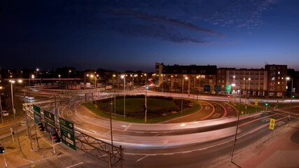Wall Mural - A city roundabout illuminated at dusk with light trails from passing vehicles, capturing the flow of traffic in a time lapse under a darkening blue sky, showcasing urban night life.