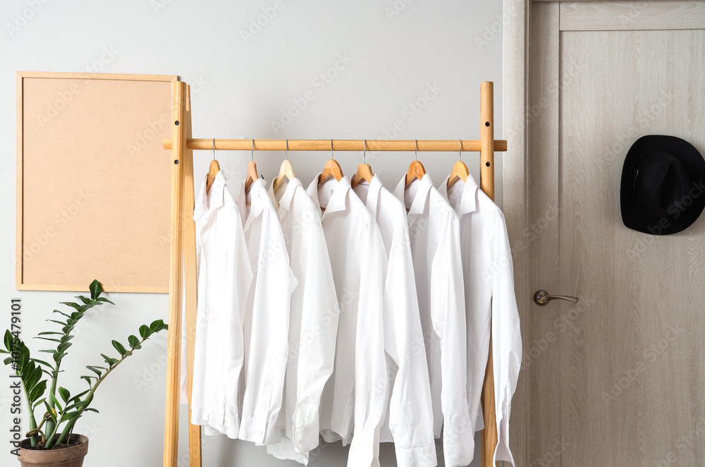 Rack with man's shirts near white wall in room