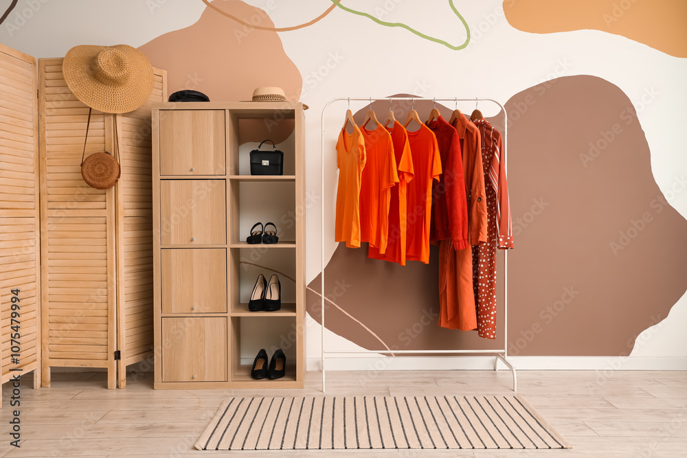 Rack with orange clothes near colorful wall in room