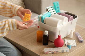 Poster - Woman taking pills with first aid kit on table at home, closeup