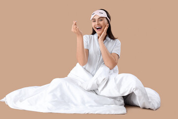 Wall Mural - Young woman in striped pajamas with blanket making heart gesture on beige background