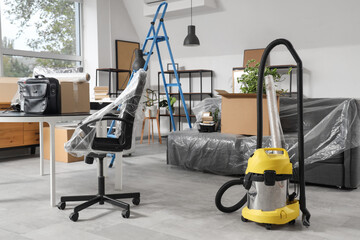 Interior of office with desk, boxes and vacuum cleaner on moving day