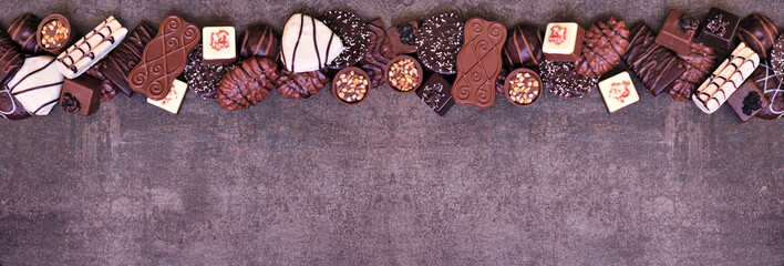 Poster - Chocolate top border with an assortment of fine, luxurious sweets. Top view on a dark stone banner background with copy space.