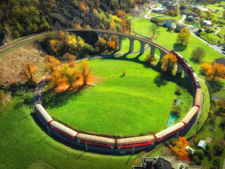 Wall Mural - aerial view of red train on kreisviadukt in alpine mountains at sunset in autumn. bernina express, s