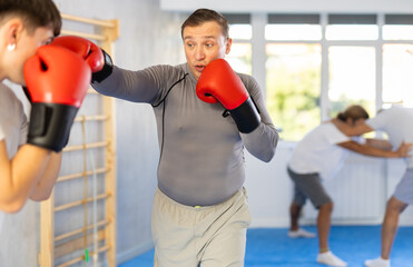 Wall Mural - Adult man with partner in boxing gloves boxing in gym..