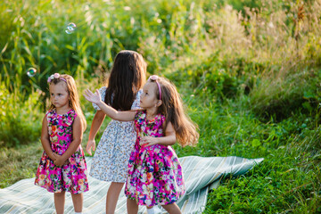 Wall Mural - Happiness, sisters children having fun together in a green garden  In Ukraine.Smiling children are playing with bubbles in the park.